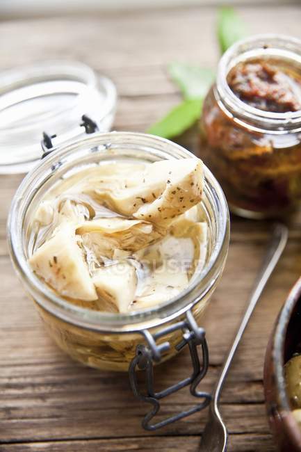Preserved artichoke hearts and dried tomatoes in jars over wooden surface — Stock Photo