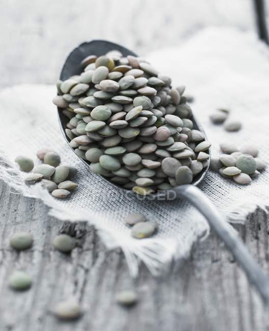 Closeup view of lentils on a spoon, cloth and wooden surface — Stock Photo