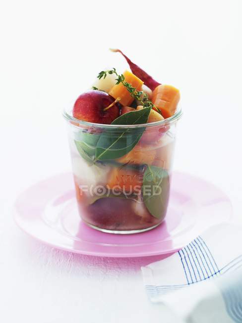 Ein Arrangement aus Gemüse, Apfel und Kräutern in einem Glas über rosa Teller — Stockfoto
