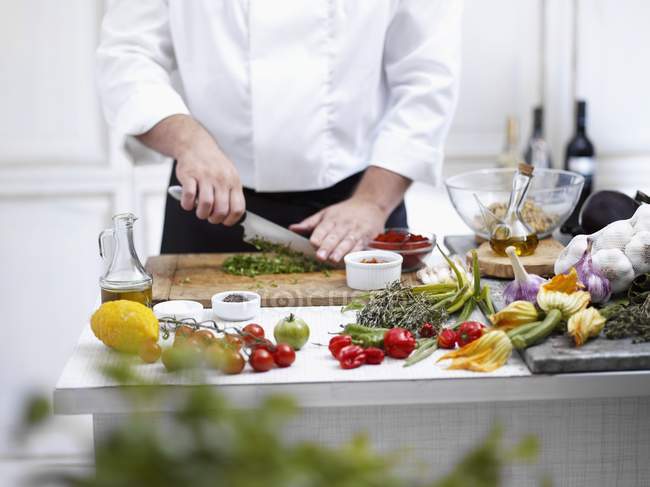 Chef rebanando verduras con cuchillo en las manos sobre escritorio de madera, sección media - foto de stock