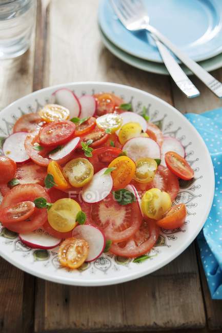 A colourful tomato salad with radishes on white plate over wooden surface — Stock Photo