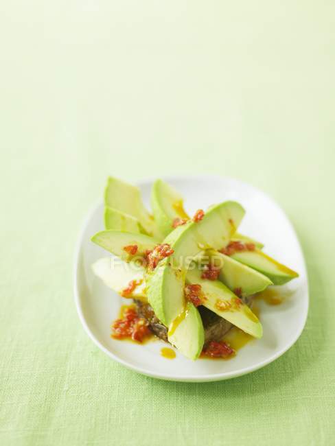 Avocado con salsa piccante su piatto bianco su superficie verde — Foto stock