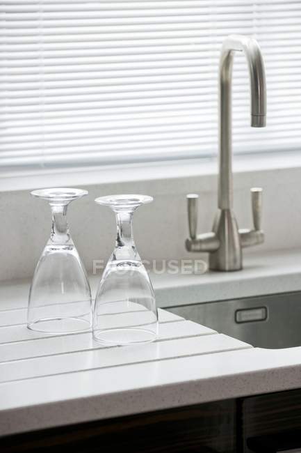 Deux verres à tige sur une planche à drainer en quartz poli à côté d'un évier avec un robinet moderne en acier inoxydable — Photo de stock