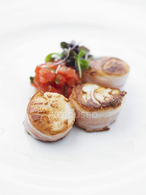 Three fried scallops wrapped in bacon with tomato tartar and shiso cress  on white surface — Stock Photo