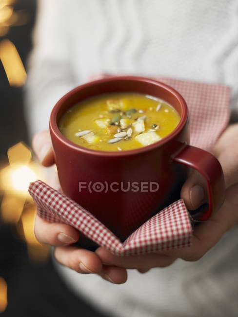 Mani che tengono la tazza di zuppa di zucca — Foto stock