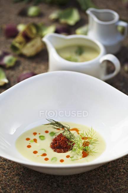 Crema de sopa de alcachofa con chorizo y guisantes en plato blanco - foto de stock