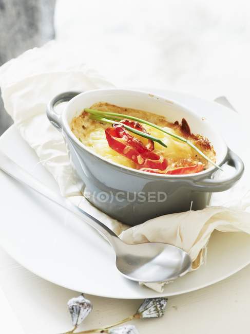 A mini potato gratin in bowl  over towel with spoon — Stock Photo