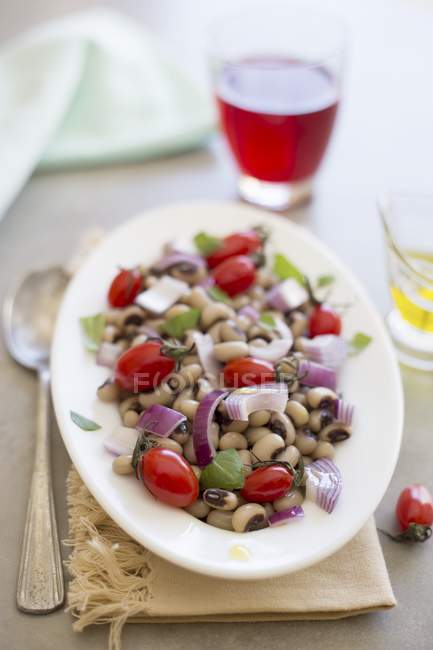 Салат из гороха с помидорами и красным луком на белой тарелке поверх полотенца — стоковое фото