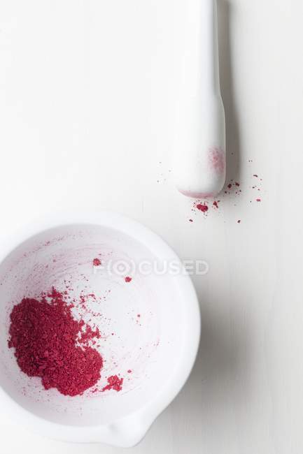 Closeup view of crushed dried raspberries in a white mortar with a pestle — Stock Photo