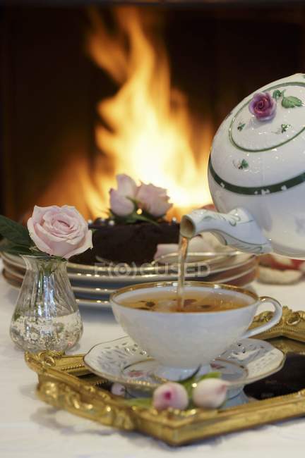 Closeup view of pouring tea by chocolate cake in front of open fire — Stock Photo