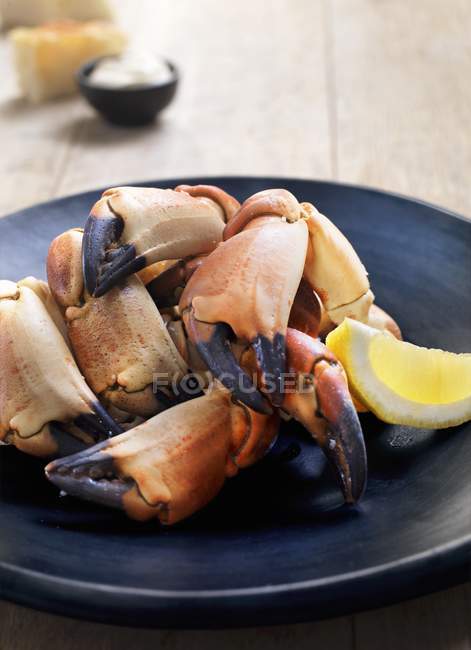 Lobster claws with lemon on black plate — Stock Photo