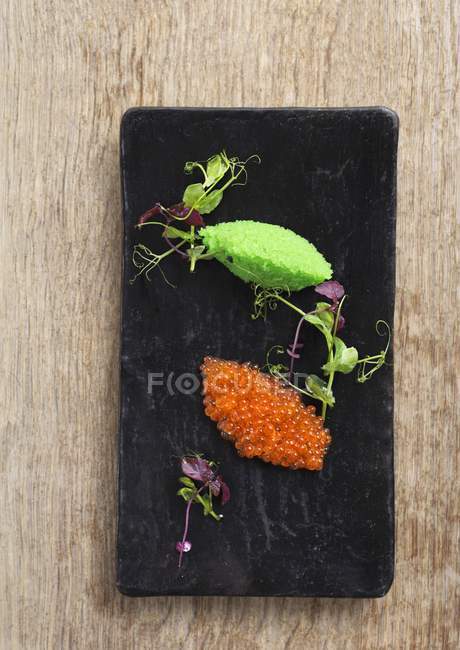 Top view of orange and green fish roe with herbs on black board — Stock Photo