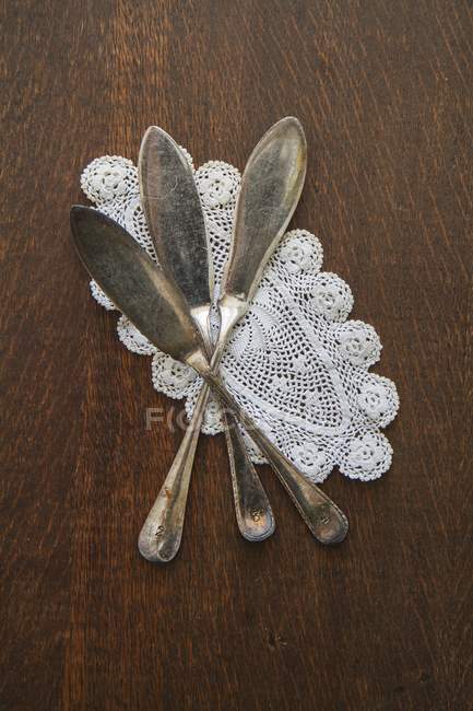 Top view of fish knives on doily and dark brown wooden surface — Stock Photo