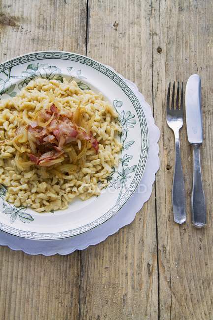 Sptzle -soft egg noodles with bacon and onions on plate over wooden surface — Stock Photo
