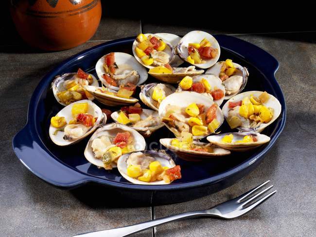 Clams filled with sweetcorn and tomatoes on black plate — Stock Photo