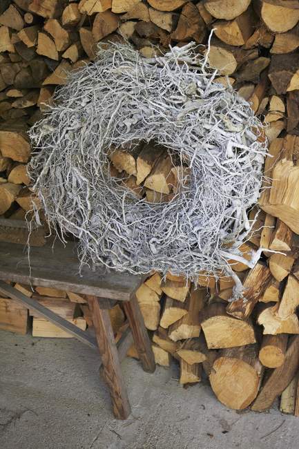 Tagesansicht eines geflochtenen Kranzes auf einer Bank vor einem Holzstapel — Stockfoto