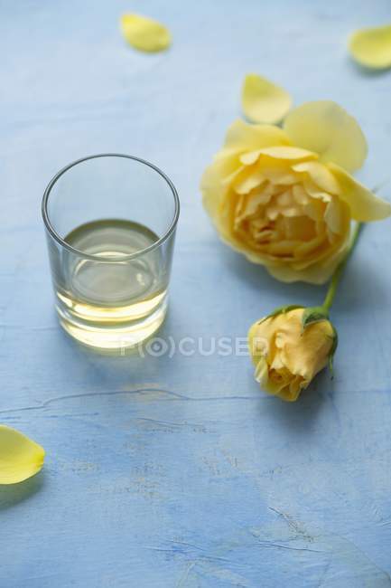 Vue rapprochée de l'eau de rose et d'une rose jaune sur la surface bleue — Photo de stock
