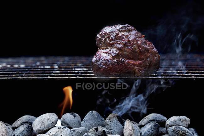 Вид крупным планом на кусок курицы на стойке для барбекю над углями — стоковое фото