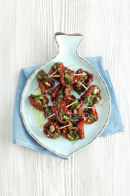 Dried tomatoes filled with capers, anchovies and parsley on blue plate over towel — Stock Photo