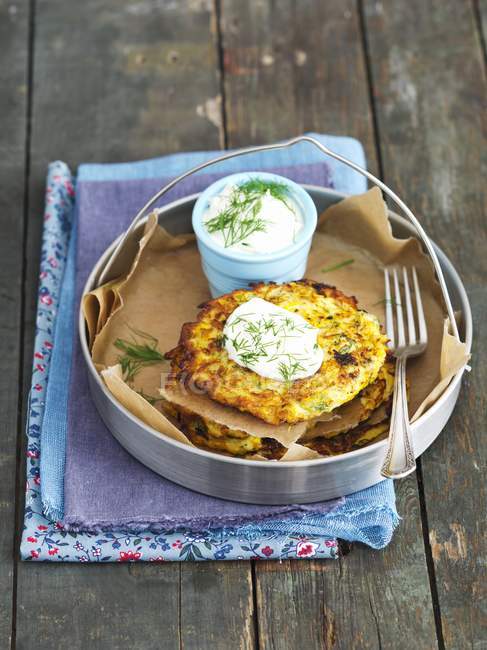Yellow courgette fritters with sour cream and dill in dish over wooden surface — Stock Photo