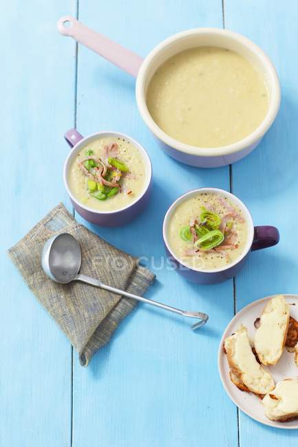 Cream of leek soup with ham over blue wooden surface — Stock Photo