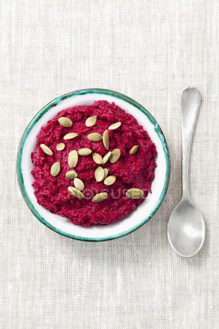 Beetroot spread with pumpkin seeds on blue plate over table with spoon — Stock Photo