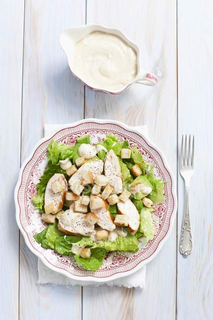 Caesar salad with avocado, chicken and croutons on plate over wooden surface — Stock Photo
