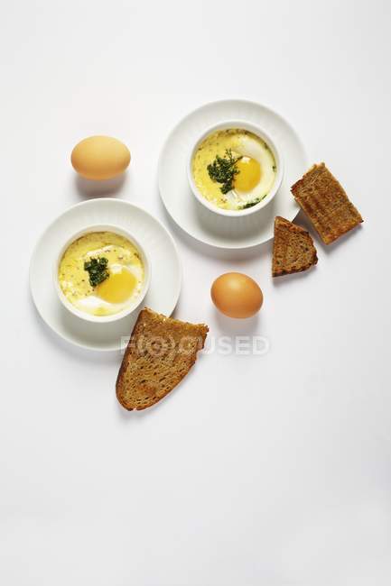 Vista dall'alto di Oeufs en cocotte con erbe primaverili, uova e pane tostato — Foto stock