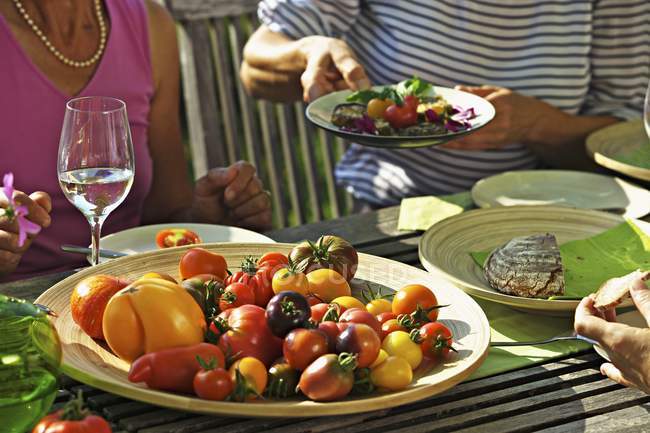 Les gens qui mangent des tomates à une table de jardin en été, section médiane — Photo de stock
