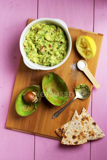 Guacamole com ingredientes em mesa de madeira com tigela — Fotografia de Stock