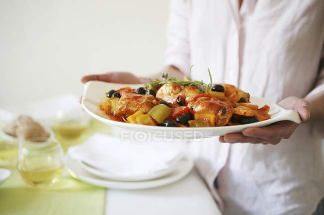 Pfefferhuhn mit schwarzen Oliven auf Teller in Frauenhand, Mittelteil — Stockfoto