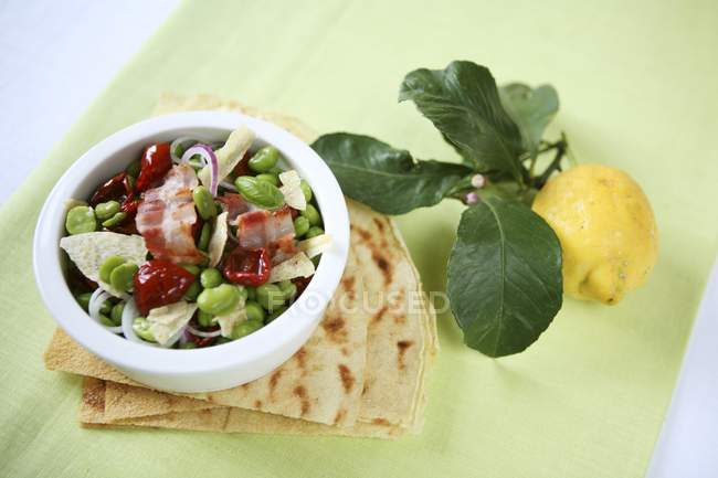 Insalata di fave - бобовий салат із сушеними помідорами та беконом у білій страві — стокове фото