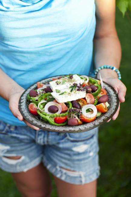 Frau hält Teller mit griechischem Salat — Stockfoto