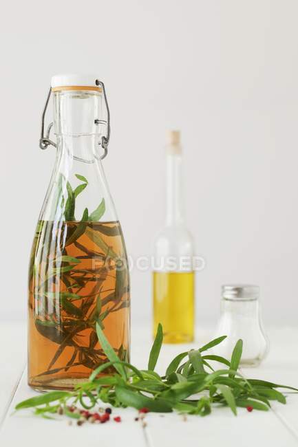 Vista de cerca de una botella de vinagre de estragón, estragón fresco y granos de pimienta - foto de stock