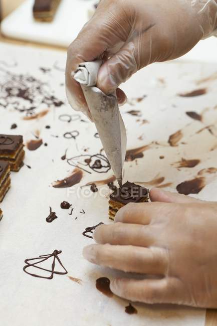 Primo piano vista ritagliata di pasticceria decorare un Petit quattro con cioccolato — Foto stock