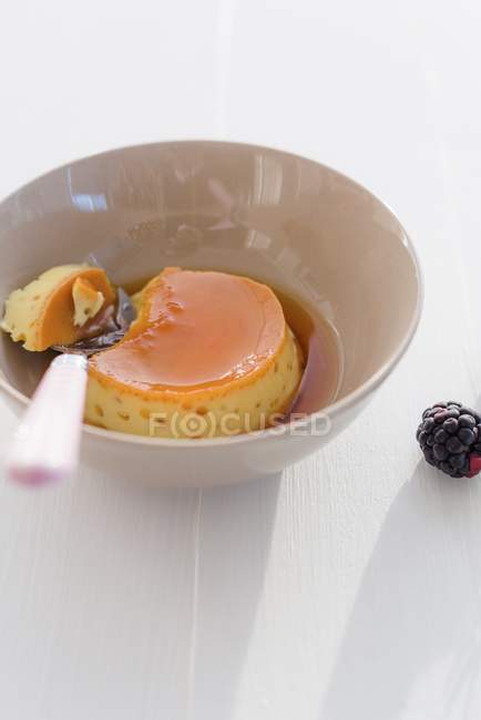 Vue rapprochée du caramel crème avec cuillère dans un bol et une mûre sur la surface blanche — Photo de stock