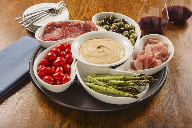 Hummus dip with ham, salami, olives and vegetables in bowls — Stock Photo
