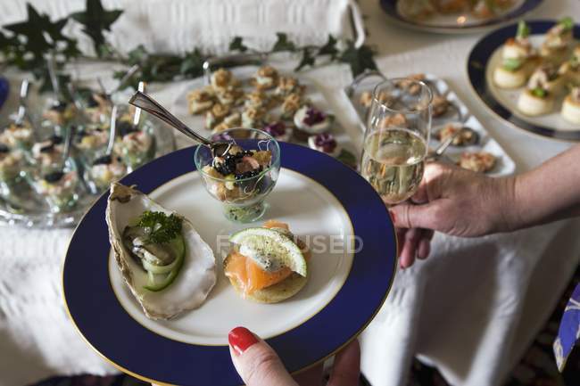 Cropped view of woman holding seafood appetizers on plate and glass of wine — Stock Photo