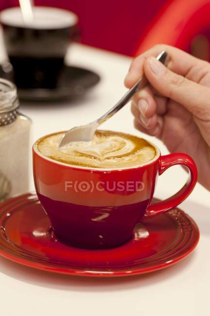 Hand stirring a hot cappuccino — Stock Photo