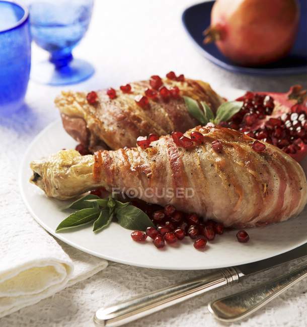 Closeup view of turkey legs wrapped in bacon with pomegranate seeds and sage — Stock Photo