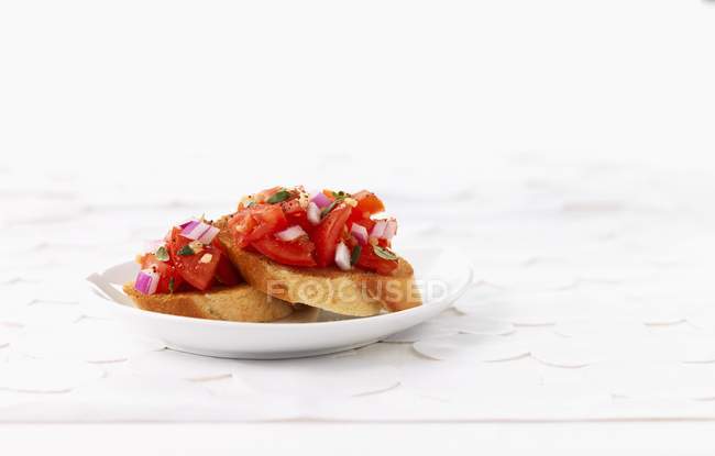 Bruschetta condita con pomodori e cipolle su piatto bianco — Foto stock