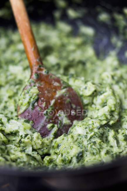 Creamy spinach in a pan with a wooden spoon — Stock Photo