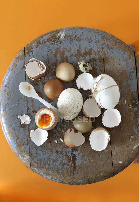 Вид зверху на різні яйця, яєчні мушлі і м'яко зварене яйце на старовинному табуреті — стокове фото