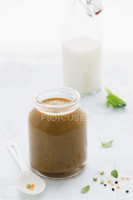 A glass jar of baby lentil pure with a bottle of milk in the background — Stock Photo