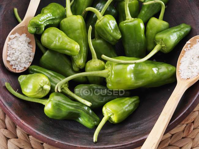 Fresh pimientos with sea salt on brown plate with wooden spoons — Stock Photo