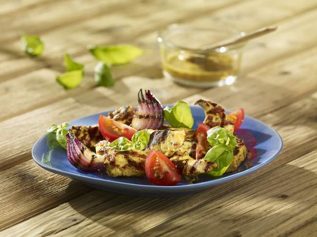 Куриные полоски на гриле с луком и помидорами на голубой тарелке — стоковое фото