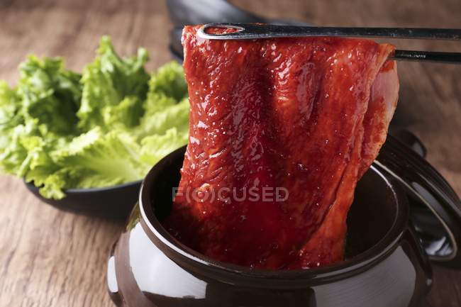 Raw marinated beef in pair of tongs — Stock Photo