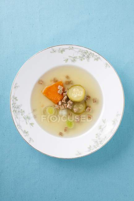 Caldo de verduras transparente en plato blanco sobre superficie azul - foto de stock