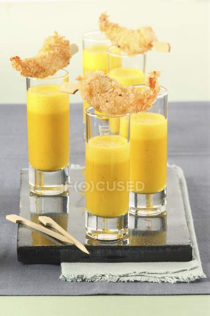 Orange and pumpkin soup shots with scampi over desk wih glases — Stock Photo