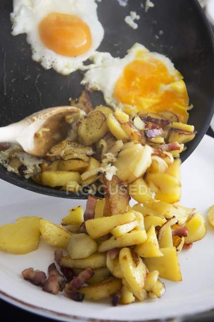 Bratkartoffeln mit Speck und Spiegeleiern auf weißem Teller — Stockfoto
